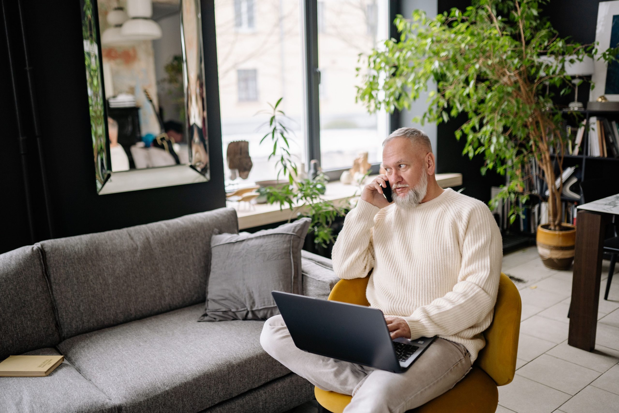 Homme age utilisant laptop et telephone a domicile